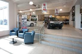 Hunt Club Honda showroom with freshly painted light walls, display vehicle, blue lounge chairs, glass railing, tiled steps, and large showroom windows.