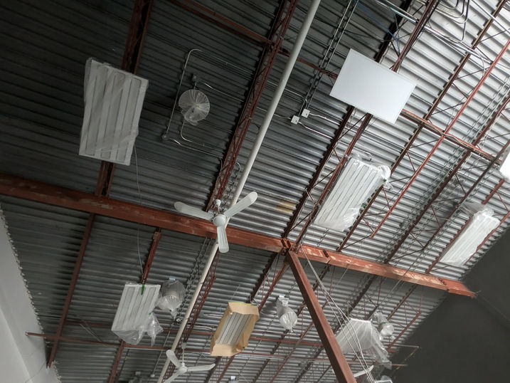 Before photo of Wellspring Studios warehouse painting project in Nepean, Ontario, showing the original exposed ceiling with steel beams, roof deck, ductwork, piping, protected lighting fixtures and preparation for spray painting.