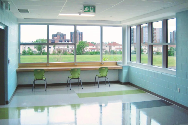 St. Patrick’s High School student seating area with freshly painted light blue block walls, large corner windows, green chairs, built-in counter, and polished school flooring.