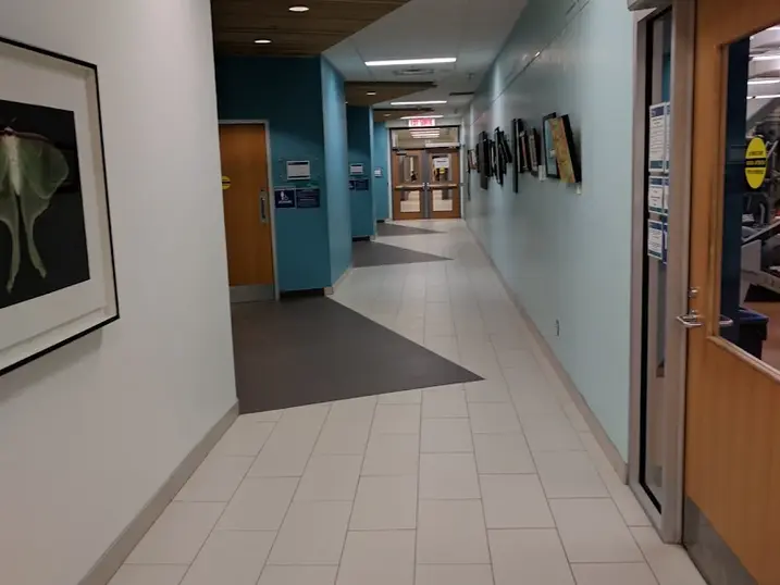 Francois Dupuis Recreation Centre corridor with freshly painted light walls, blue accent wall, tiled flooring, wood door, artwork, and bright ceiling lights.