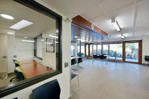 Apartment building common area with freshly painted light walls, large interior window, seating area, wood ceiling feature, and glass entrance doors.