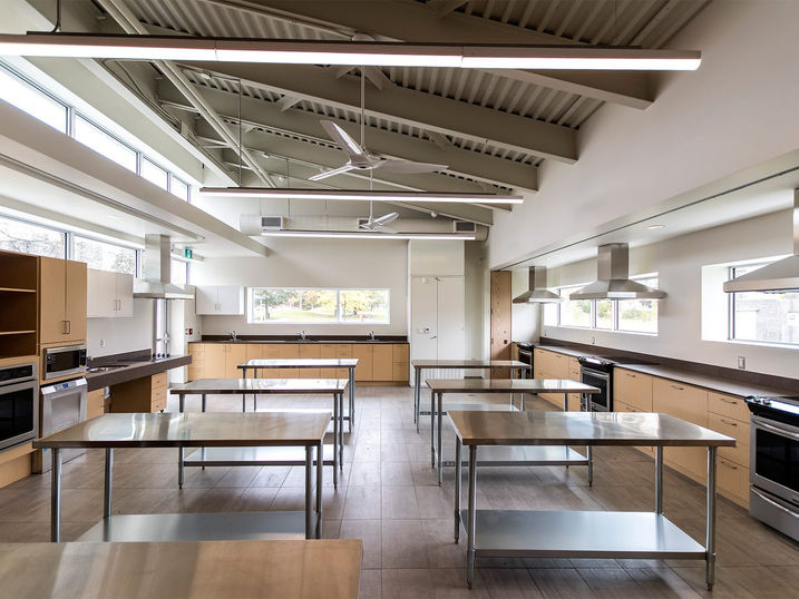 Albion-Heatherington Community Centre kitchen with freshly painted white walls, exposed ceiling structure, stainless steel worktables, wood cabinets, appliances, and bright overhead lighting.