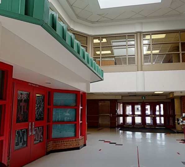 St. Mark Catholic School student atrium with freshly painted light walls, red window frames, green upper railing, large interior windows, and polished school flooring.