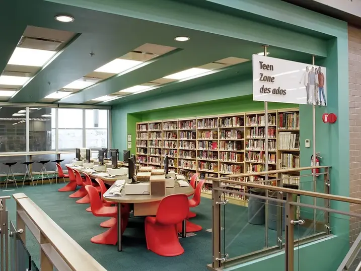 Greenboro Library teen zone with freshly painted green walls and ceiling bulkheads, bookshelves, study tables, red chairs, and glass railings.