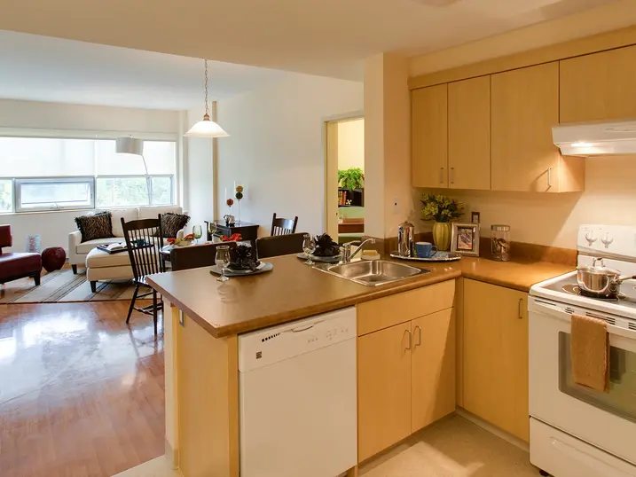 Health centre residential suite with freshly painted light walls, kitchen cabinets, white appliances, wood flooring, and a bright living area.