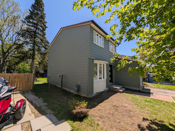 Side view of a two-storey house with freshly painted green siding and brick, white trim and shutters, black front door, and updated exterior finishes.