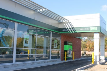 TD Canada Trust branch exterior with large glass windows, green brand signage, drive-thru entrance, brick façade, and modern commercial building details.