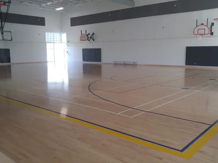 Francois Dupuis Recreation Centre gymnasium with freshly painted light walls, dark accent panels, basketball hoops, wood sports flooring, and bright overhead lighting.