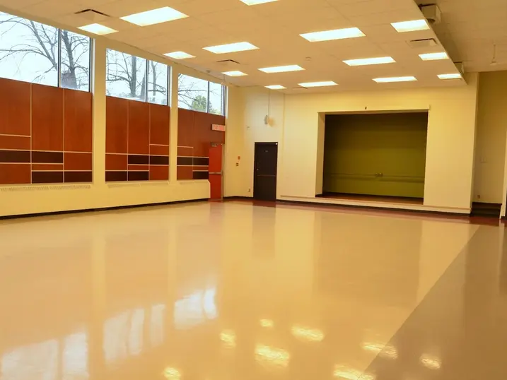 Overbrook Community Centre multi-purpose room with freshly painted light walls, orange accent panels, stage area, large windows, polished floor, and bright ceiling lights.