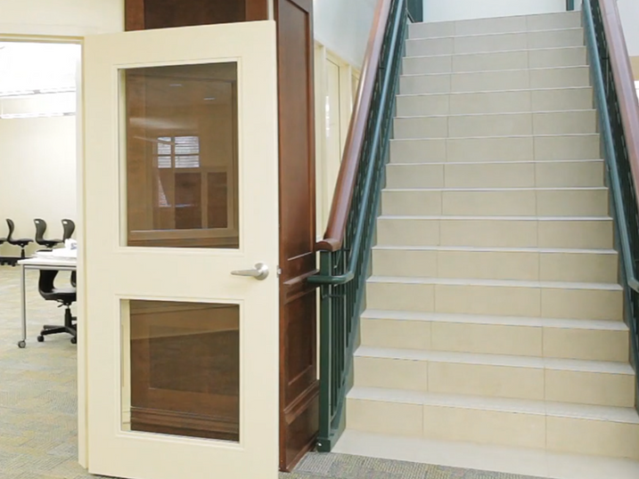 Asbury College stairwell area with freshly painted light walls, painted door frame, glass-panel door, stair railing, and tiled staircase.