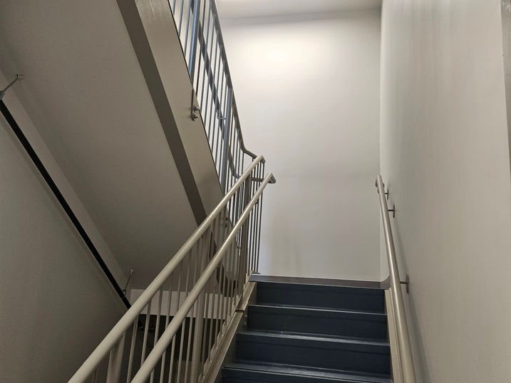 Salus Capilano stairwell with freshly painted light walls, painted metal railings, dark stairs, landing area, and bright overhead lighting.