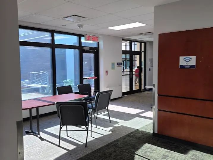 Overbrook Community Centre meeting area with freshly painted light walls, warm wood accent panel, glass doors, tables, chairs, carpet flooring, and bright natural light.