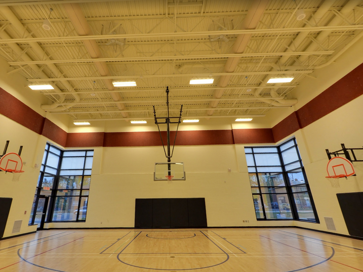 Overbrook Community Centre gymnasium with freshly painted white steel deck ceiling, warm accent wall band, basketball hoops, wall padding, tall windows, and wood sports flooring.