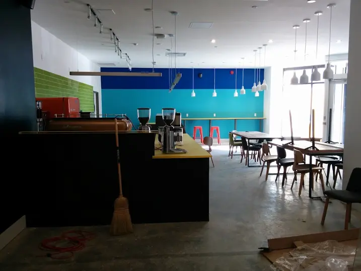 111 Cooper Street student dining area with freshly painted teal and blue accent walls, orange ceiling detail, pendant lights, tables, chairs, and service counter.