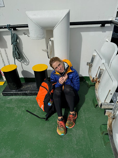 A woman in blue jacket sits with a backpack on the deck.