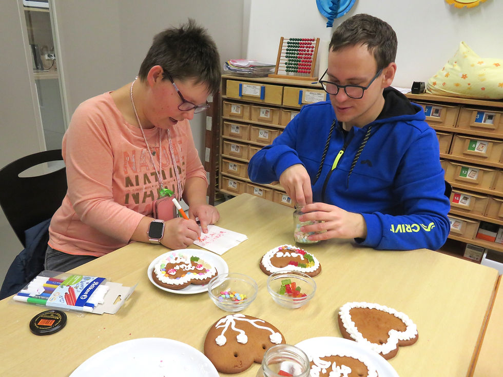 Eine Frau und ein Mann sitzen am Tisch. Verzieren Lebkuchenherzen und beschriften die Verpackungstüte