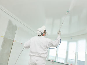 Painter worker with airless painting sprayer covering ceiling surface into white