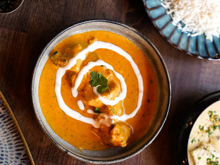 Vue du dessus du butter chicken avec du riz en plat principal, accompagné d’un curry crémeux et d’une assiette de momos, le tout servi sur une table en bois.