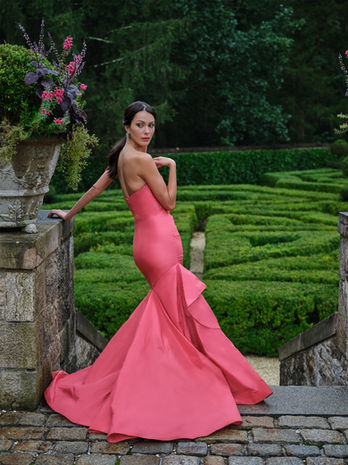 woman in strapless red taffeta ballgown standing in garden looking over her shoulder