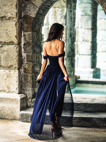 back view of woman in navy off the shoulder jumpsuit walking in garden