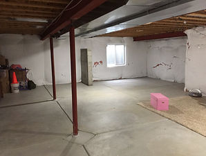 Unfinished basement with exposed ceiling joists and concrete flooring before the Saving Spaces renovation