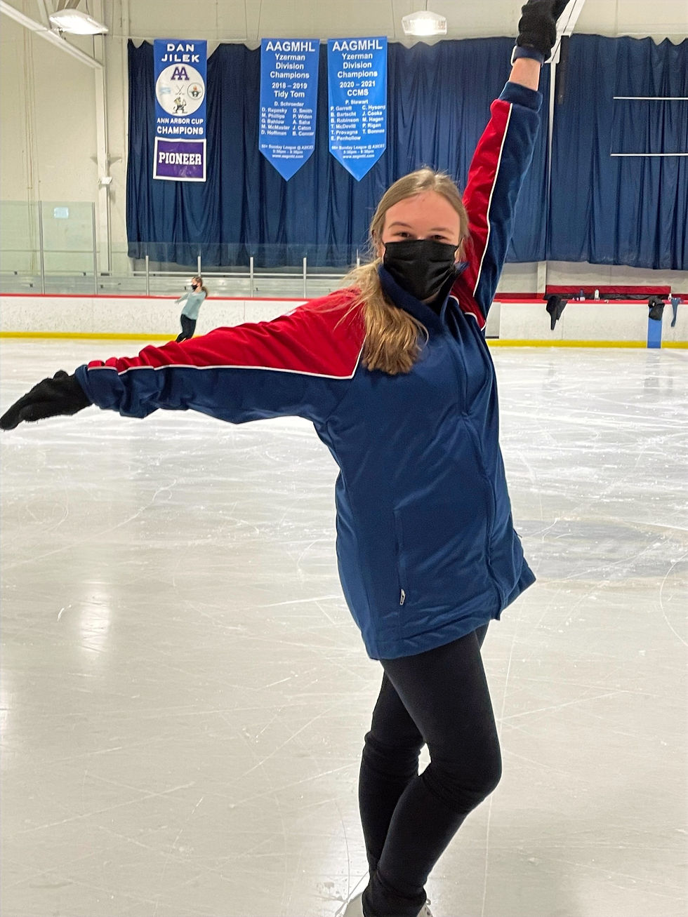 Grace poses on the ice with one arm up and one arm out to the side.