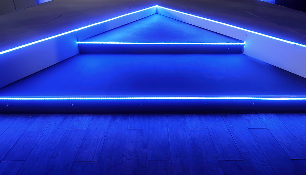 Blue-lit triangular stage with three steps, glowing neon edges, and a dark wooden floor. The setting is futuristic and moody.