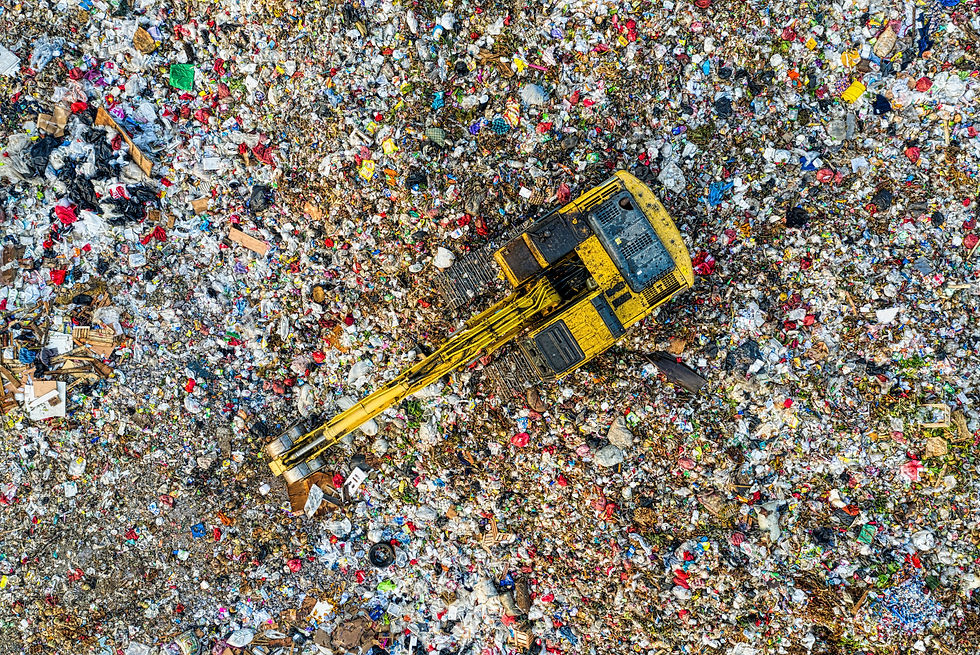 Aerial view of a yellow excavator moving through a colorful, sprawling landfill filled with trash, creating a busy, chaotic atmosphere.