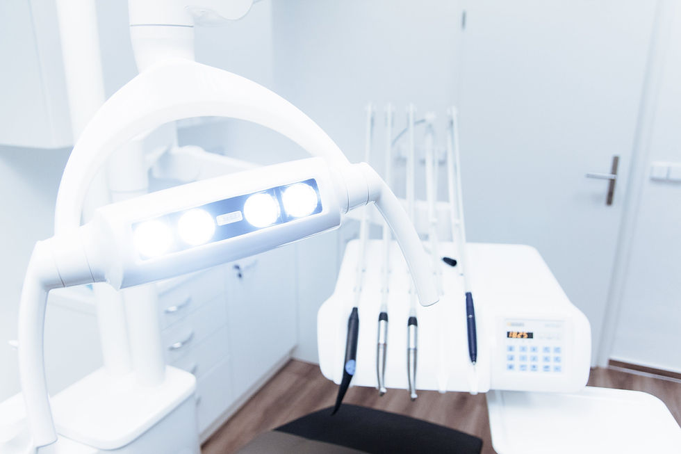 Dental office with bright exam light, dental tools on a white counter, and a modern, clean setting. Soft wood flooring in view.