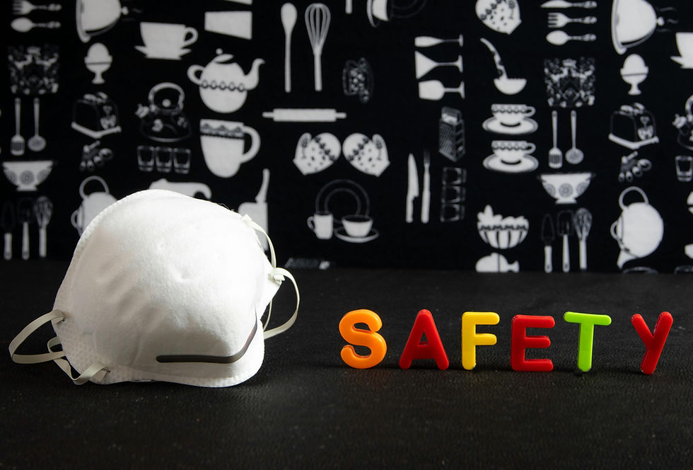 A white face mask is beside colorful magnetic letters spelling "SAFETY" on a black surface. Background has kitchen tool patterns.