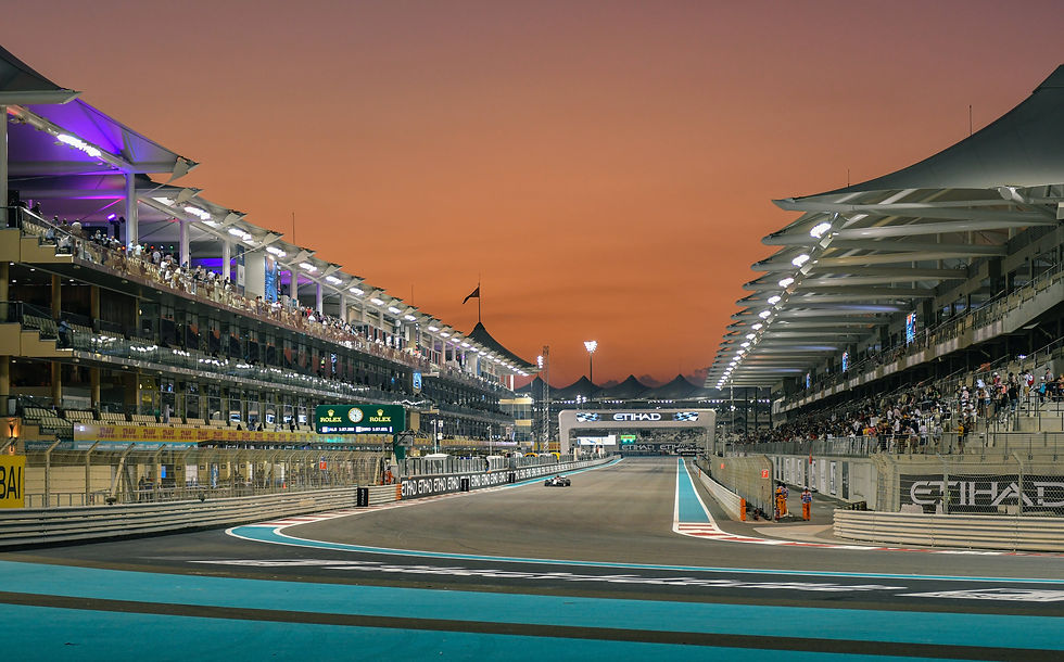 Race track at sunset with a car, spectators in stands under lit canopies, vibrant orange sky, and visible Rolex and Etihad signage.
