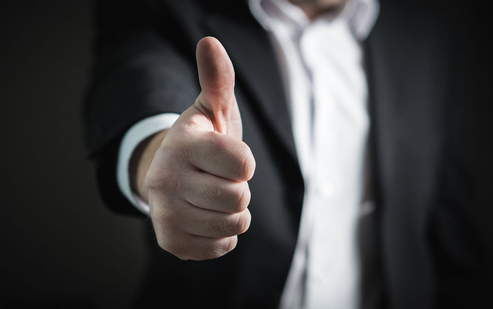 Close-up of a person in a suit giving a thumbs up against a dark background. The image conveys a positive and confident mood.