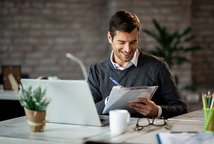Happy businessman writing notes while working on a computer in the office.jpeg