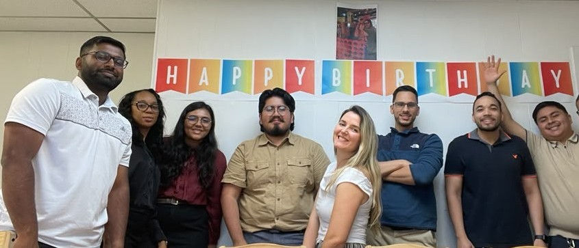 The team smiling under a Happy Birthday banner.