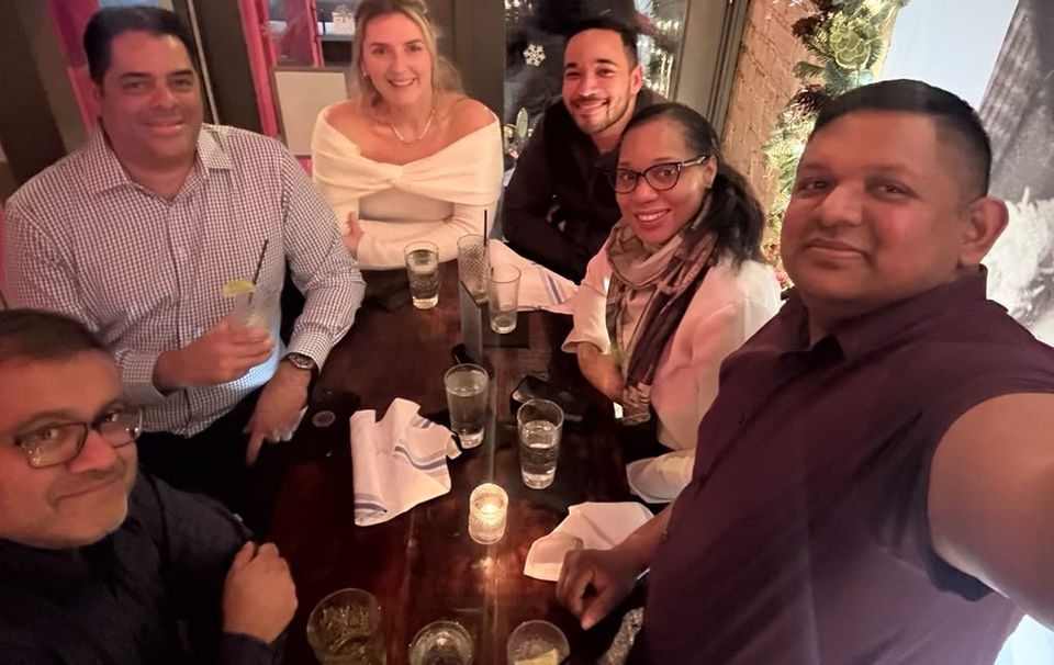 Six diverse team members smiling together at a dinner table.