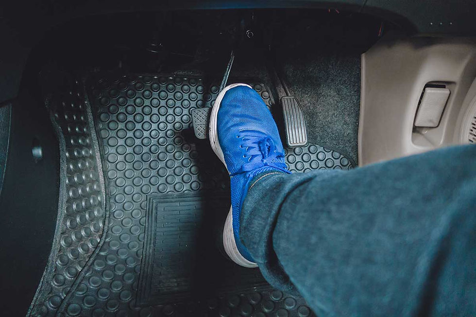 Blue sneaker presses car pedal on black rubber floor mat inside vehicle.