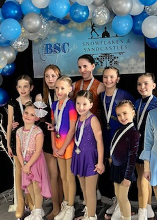 group of figure skating girls wiht medals in front of balloon arch