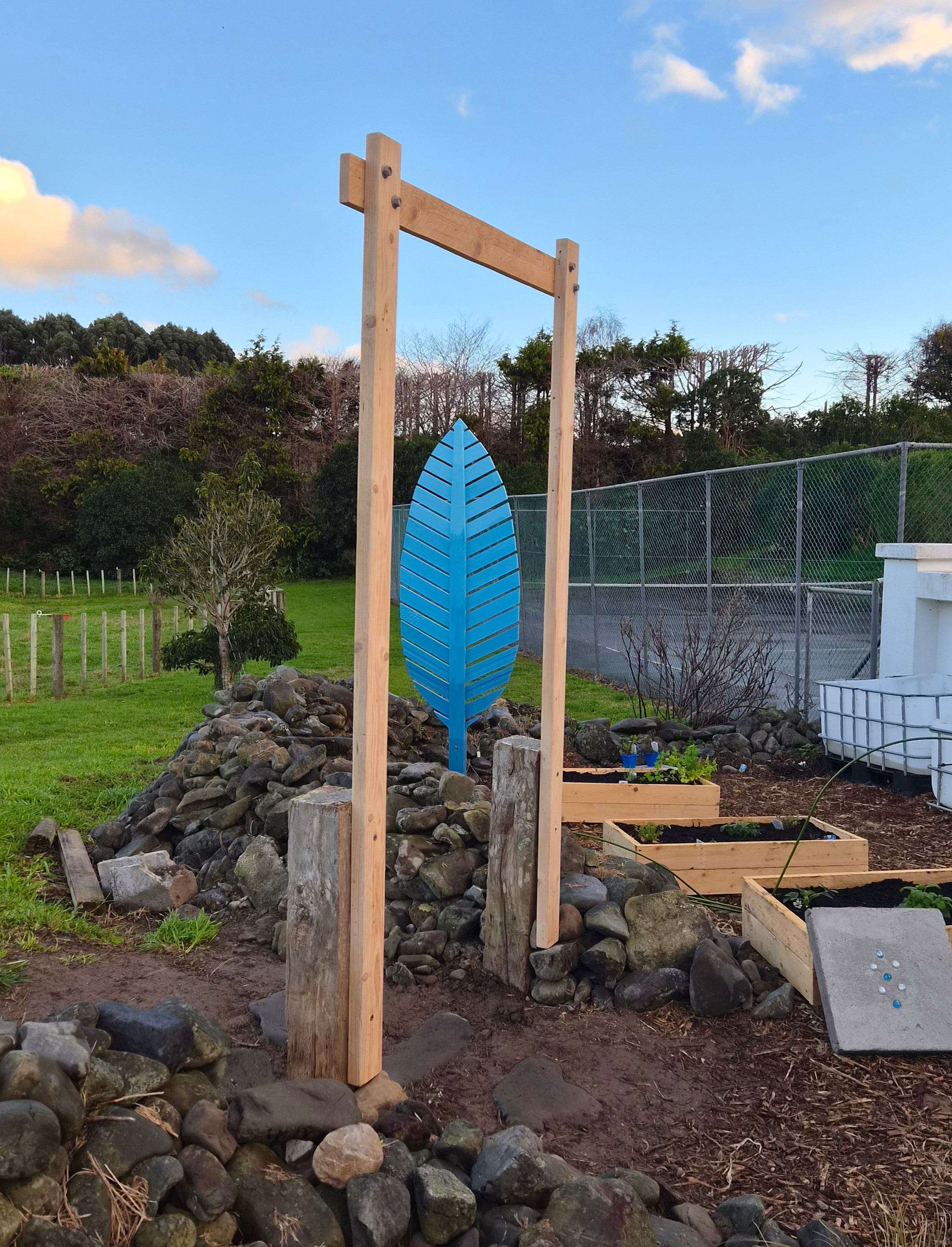 A blue leaf sculpture through a wooden garden arch