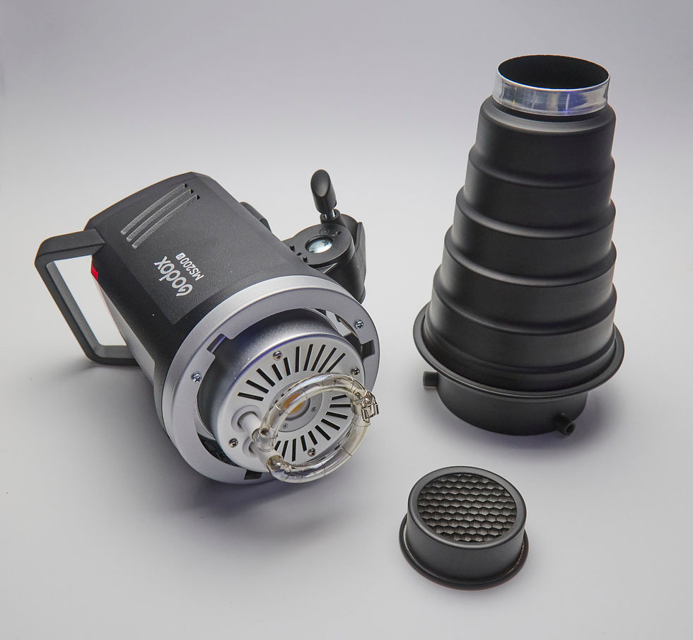 A studio flash unit lies on a white surface, next to a snoot attachment and a clip-on honeycomb grid.