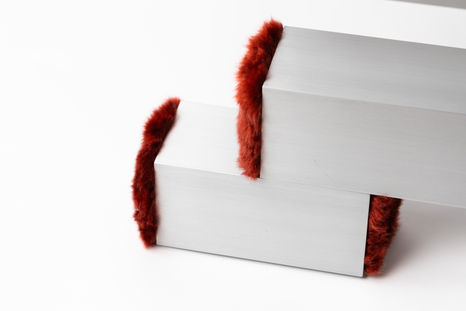 Detailed view of the brushed aluminum square tube frame with red plush fabric end caps of a designer table.