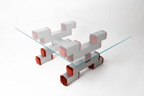 Angled top-down view of a stylish table constructed with brushed aluminum square tubes, clear glass surface, and red plush fabric end caps.
