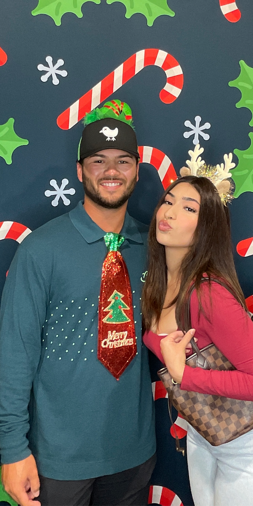 Couples taking fun Christmas photos at a Brooksville photo booth with holiday backdrop