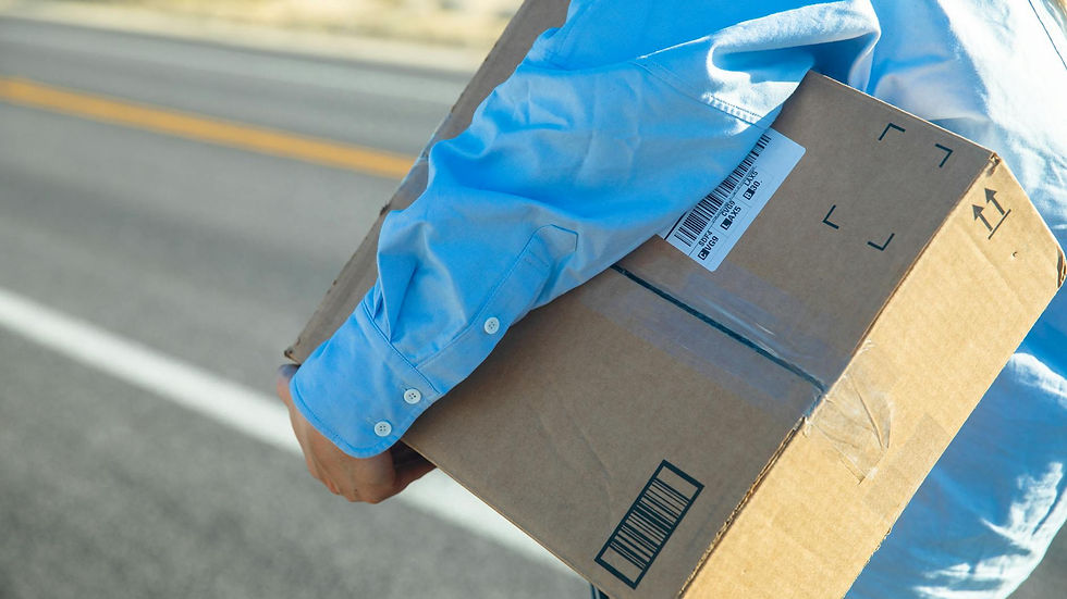 Close-up of a person carrying a cardboard box on a sunny road with a blue shirt.