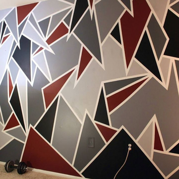 Geometric accent wall painted by DMV Walls in Maryland with a modern design of dark red, gray, and black triangles.