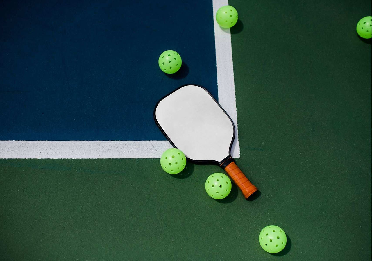 pickleball paddle with 5 balls laying on a green court
