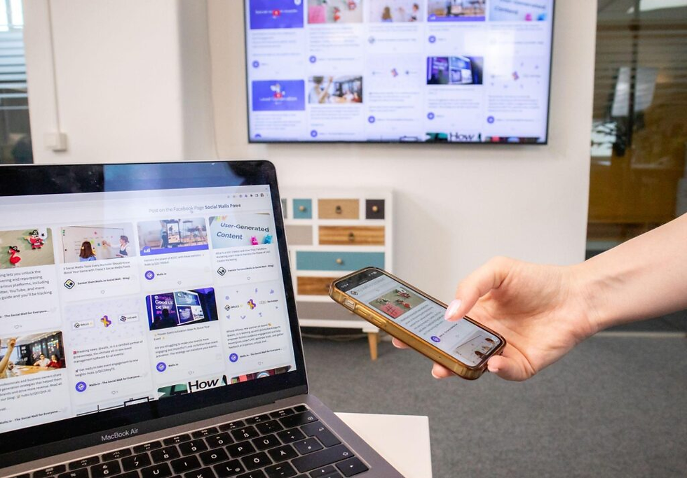 Hand holding a phone beside a MacBook Air showing Social Walls and User-Generated Content in a bright office.
