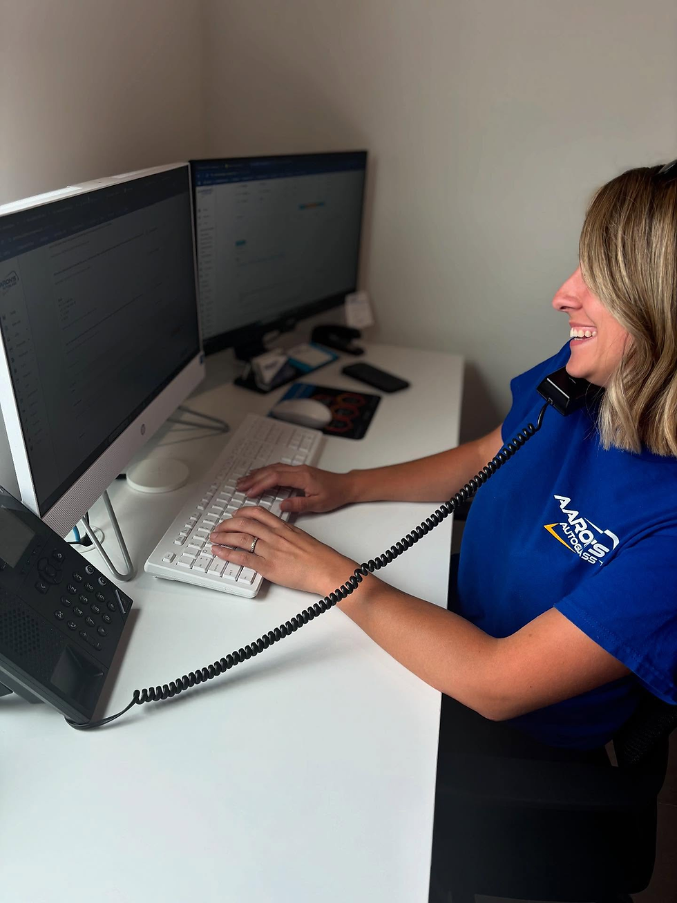 Aarons AutoGlass Service Rep Taking an insurance claim call sitting at a white desk while on the phone typing.