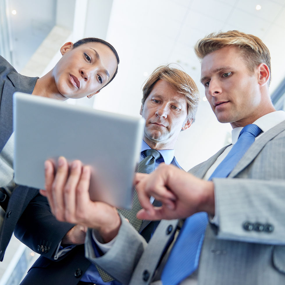 Three business professionals reviewing data on a tablet during a strategy meeting.