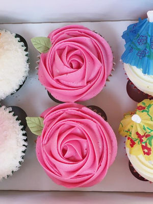 Six decorated cupcakes in a box with pink roses, umbrellas and decorations.