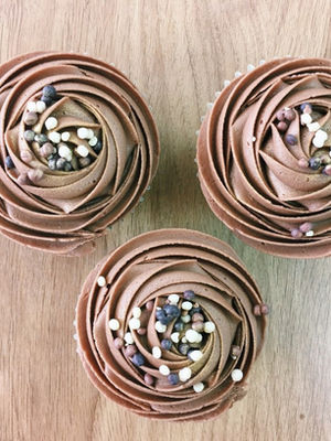 Three chocolate cupcakes with decorative frosting and sprinkles on wooden table.